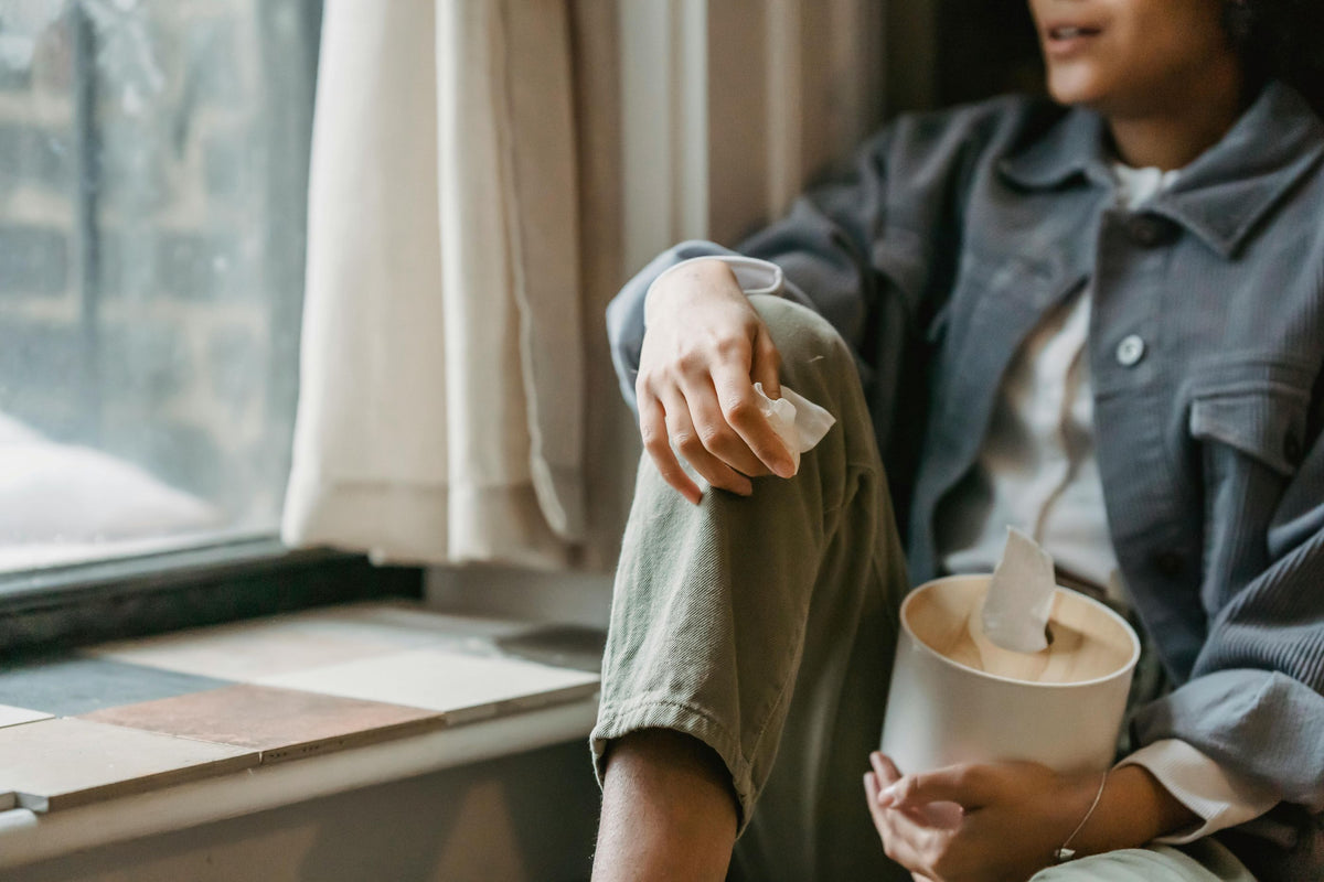 Person sitzt mit Taschentuchbox am Fenster und schaut raus